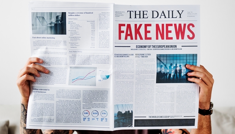 Mann hält Zeitung hoch mit Überschrift "Fake News"