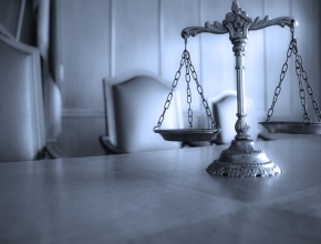 Foto mit einer Waage im Vordergrund, Gerichtssaal im Hintergrund